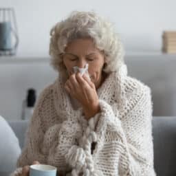Woman blowing her nose wrapped up in a blanket.